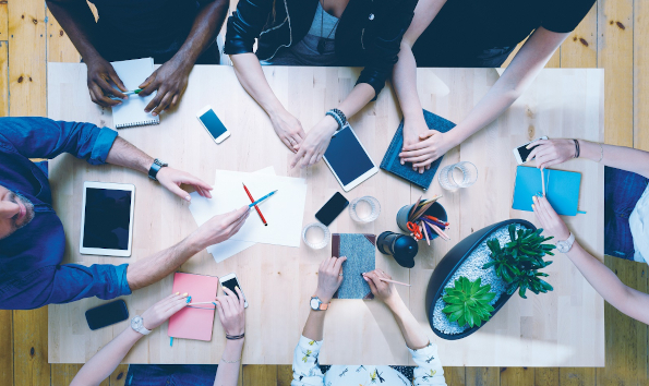 Advertising agency. High angle view of multi ethnic team of designers - caucasian and afro american - sitting at the conference table, discussing, brainstorming. Digital tablets, smart phones, notebooks on the table. Unrecognizable people.